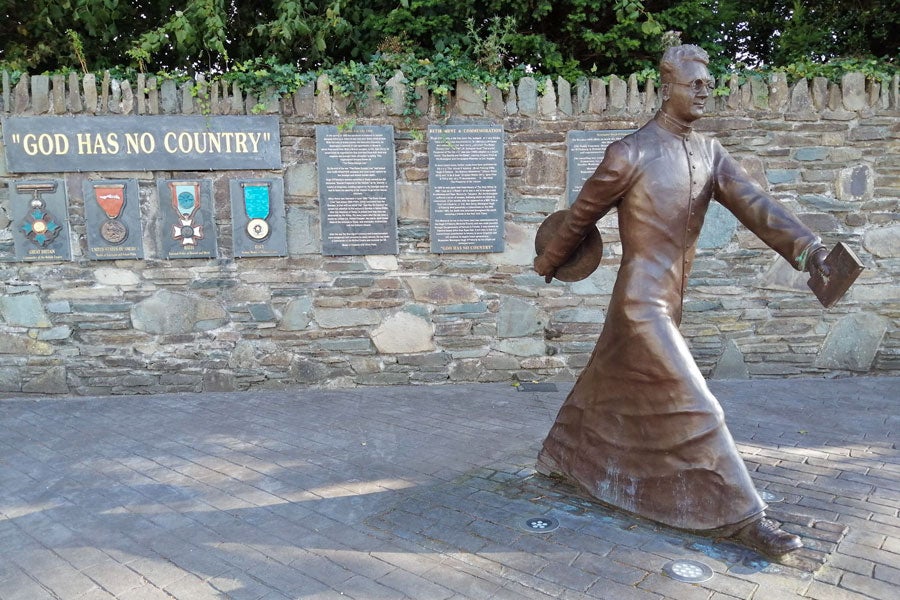Bronze statue of Monsignor Hugh O'Flaherty captured mid stride with a book in one hand and a hat in the other