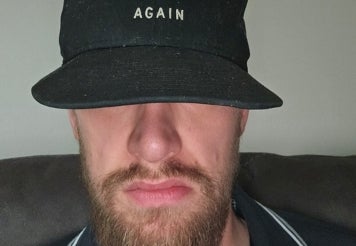 A bearded man with eyes covered by black cap.