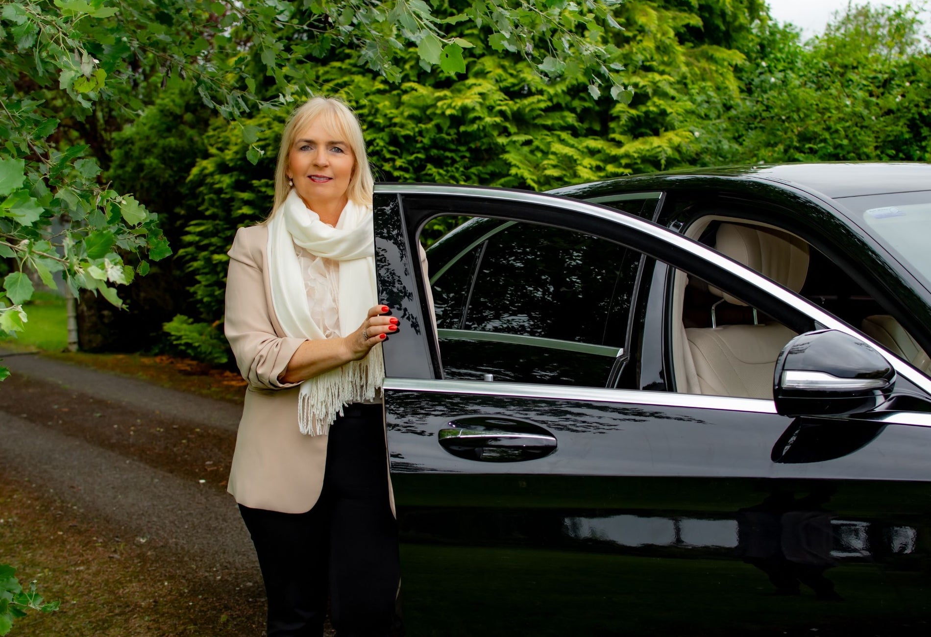 A person standing beside an open car door on a tree lined path