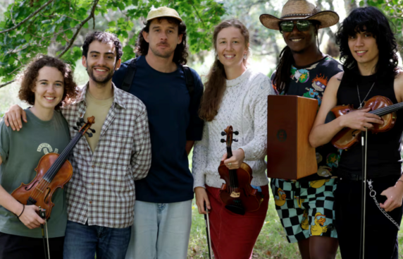 A group of 6 smiling musicians standing under trees
