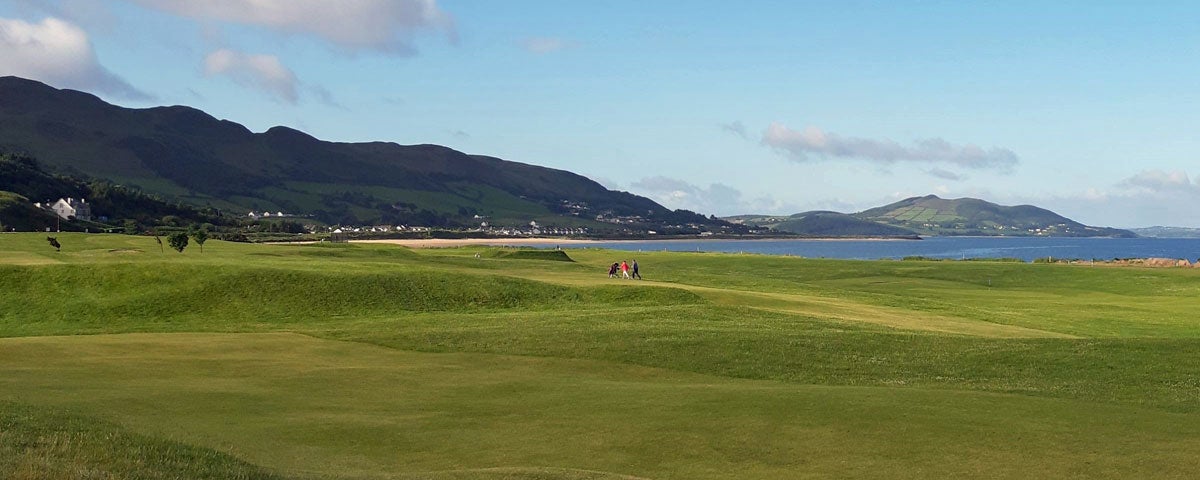 A view of the golf course with two golfers visible in the distance against a backdrop of the headland