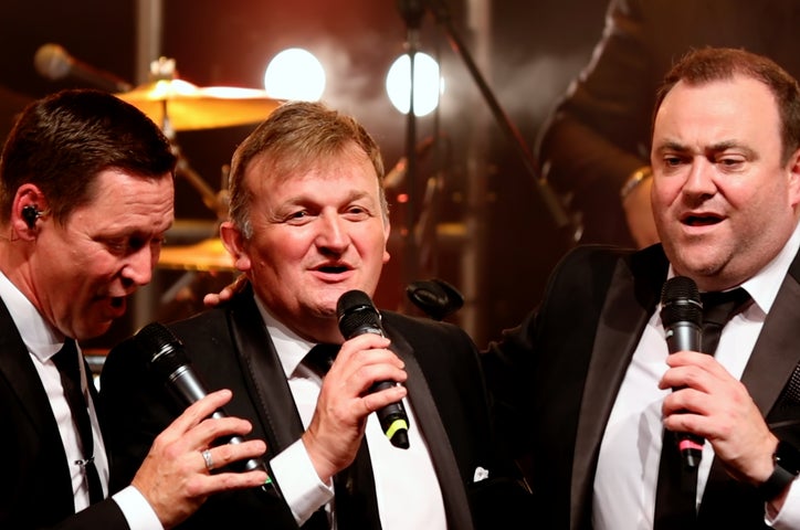 3 men in evening suits singing into mics