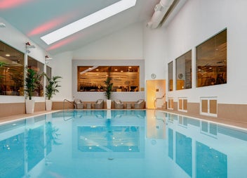 Swimming pool with wicker chairs and tables at the edge and plants