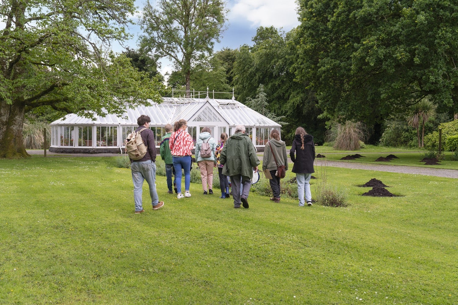 Group of people walking across a lawn to a large, white greenhouse.