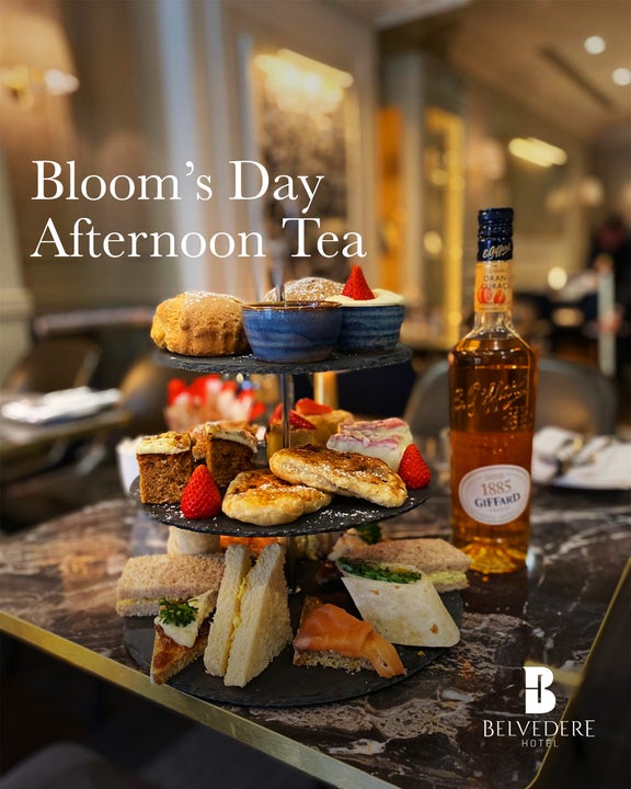 A table with stacked plates full with afternoon tea items including sandwiches, cake, scones