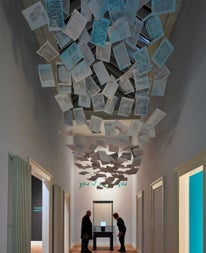 Two people looking down at an exhibit while a large exhibit of papers hangs along the ceiling above them