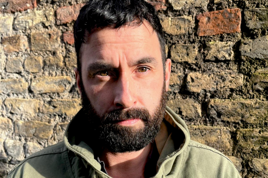 A serious looking man standing in front of a brick wall