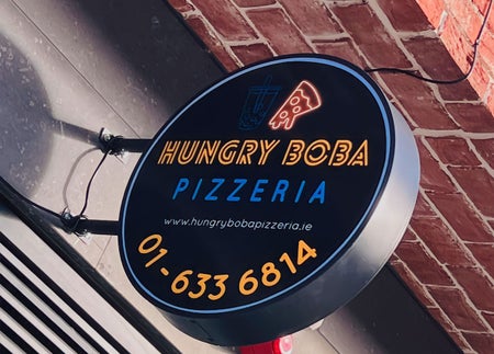 Circular sign for Hungry Boba Pizzeria with telephone number and website on display