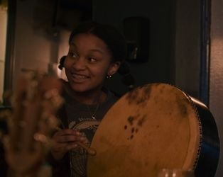 A smiling young woman playing a hand drum.