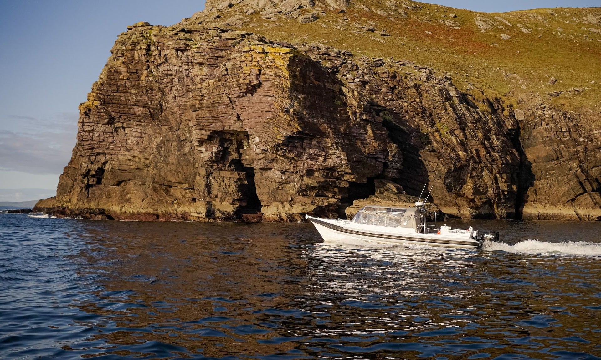 White boat in the sea cruising past a rocky cliff face