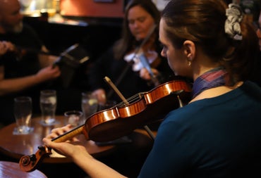 Musicians playing fiddles in a pub with empty glasses on a table