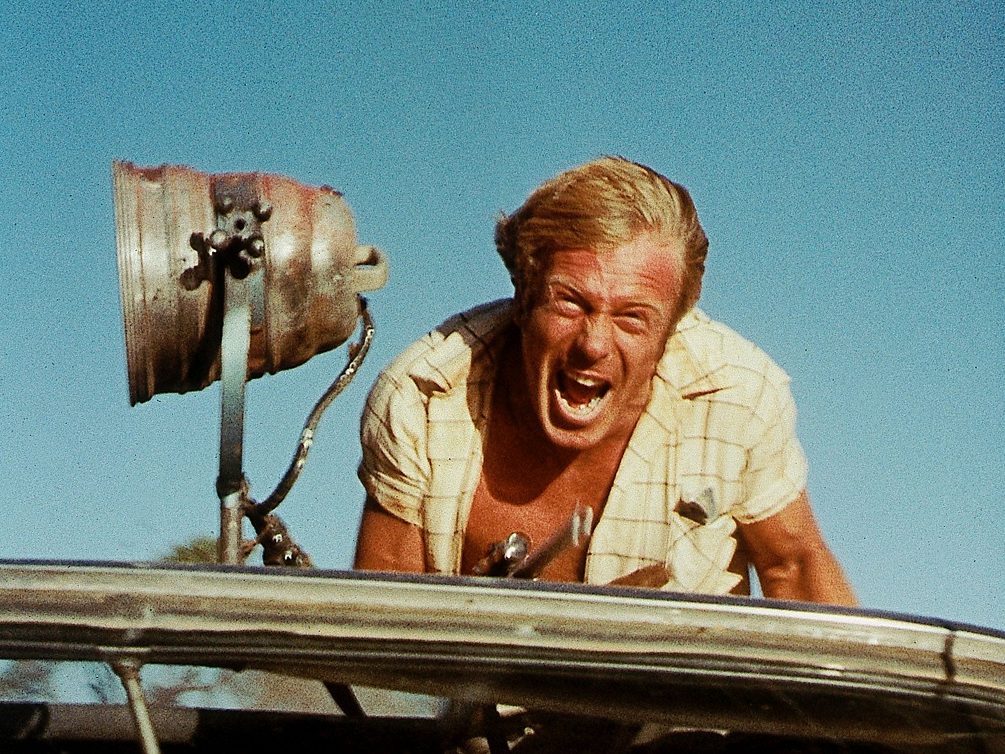 A screaming man on top of a vehicle.