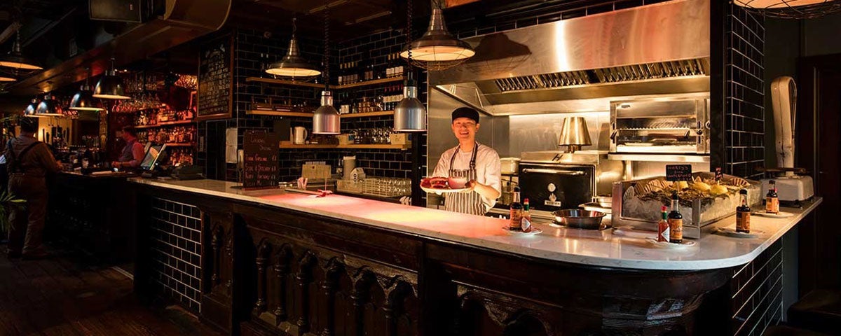 A chef standing at a work station with a plate of food