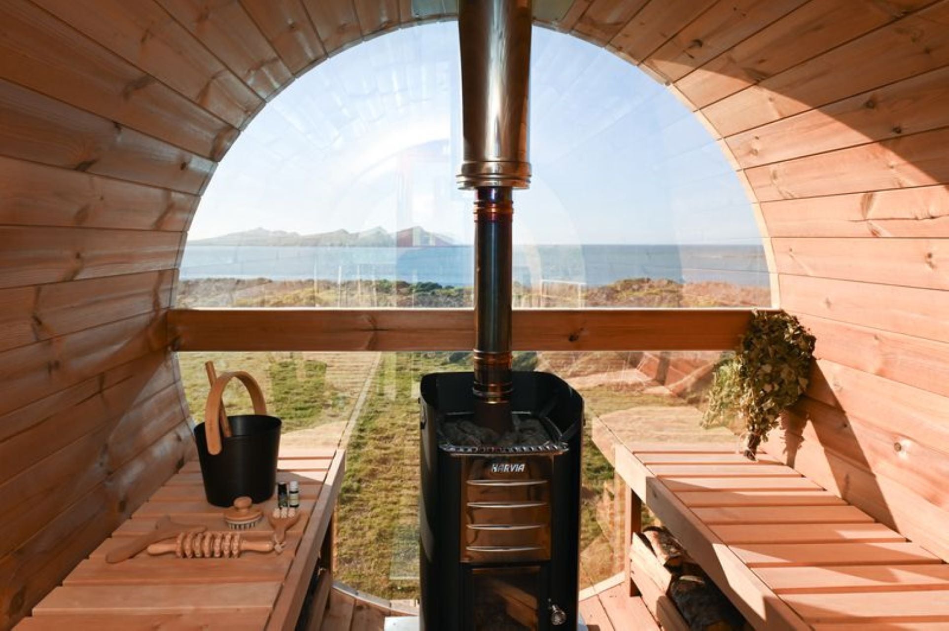 Wood burning barrel sauna interior with bench seating and Atlantic Ocean views through a large window