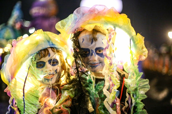 2 young people with faces painted white and dark blue with yellow large headcoverings and costumes.