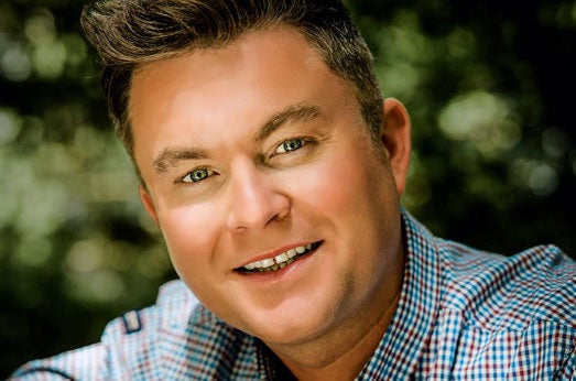 Close up of a smiling man in a small check shirt.