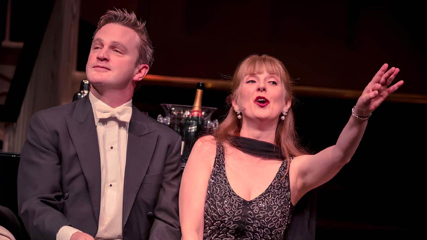 A Winter Lunchtime at the Opera, a man in evening dress beside a woman with outstretched arm, singing.
