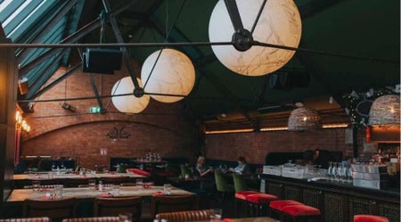 Seating area with exposed brick walls skylights globe pendant lights and a bar with red upholstered seating
