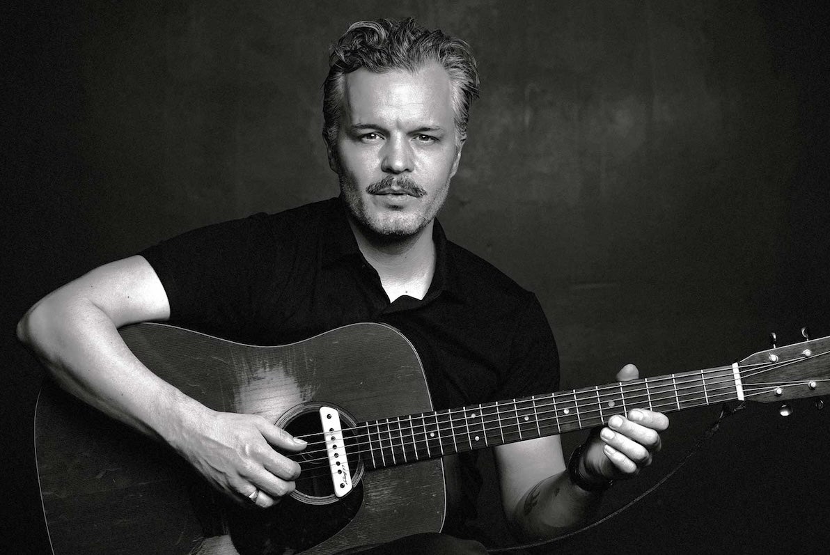 Black and white photo of man playing a guitar against plain dark background
