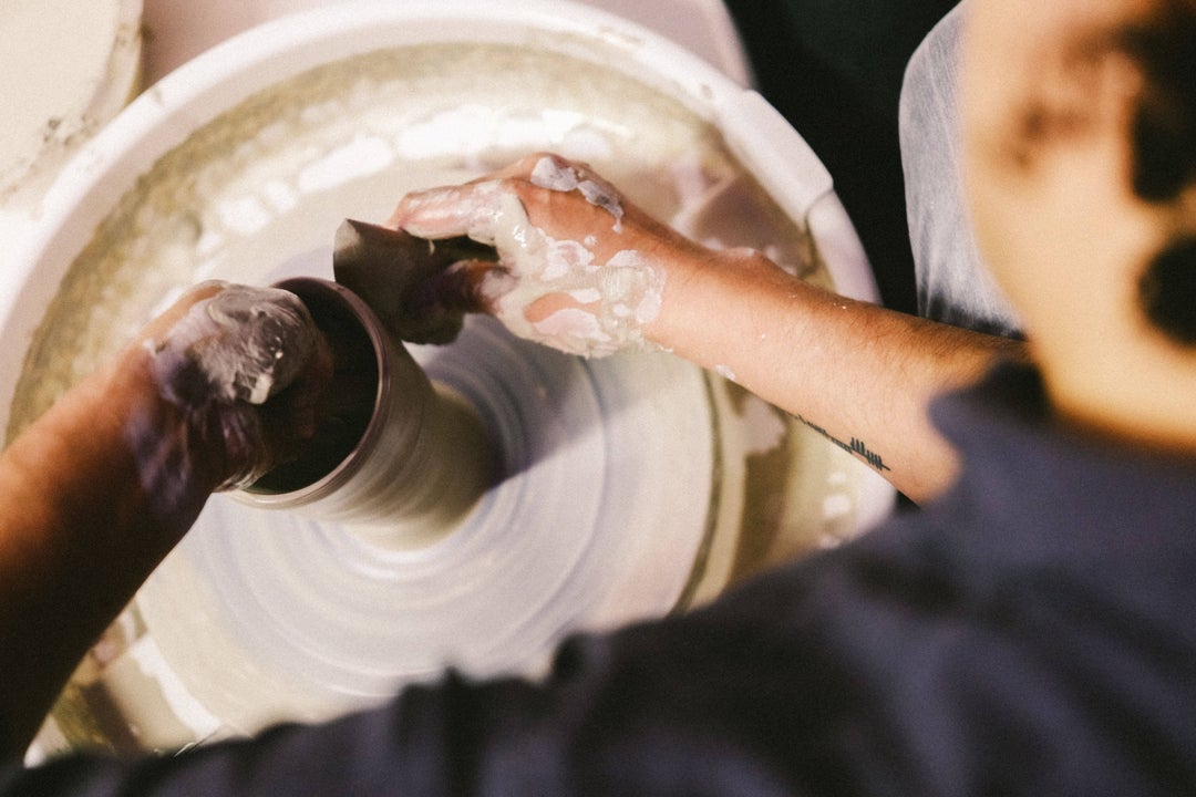 Looking down at potter's wheel with hands forming a tall pot.