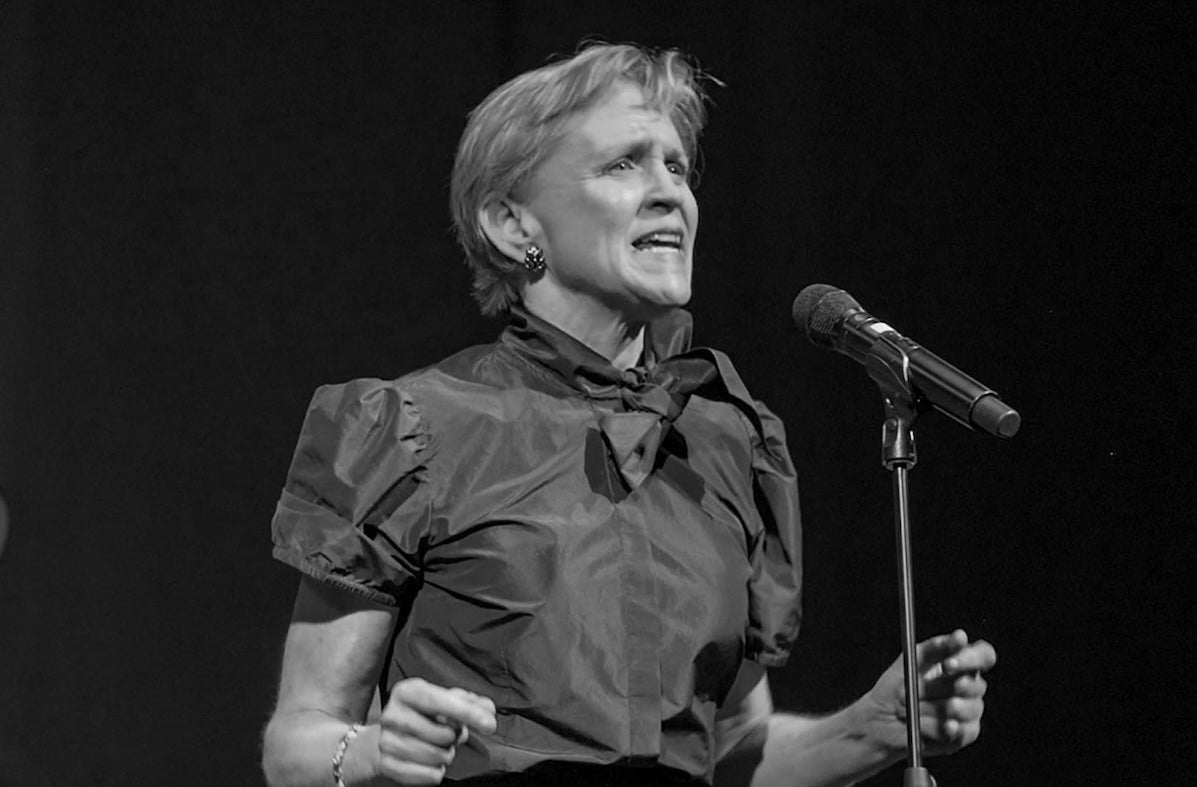 Black and white photo of woman singing with feeling into a mic on a stand.