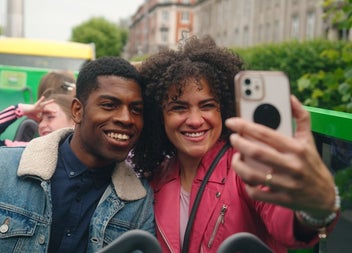 Two people sitting on an open top bus taking a selfie