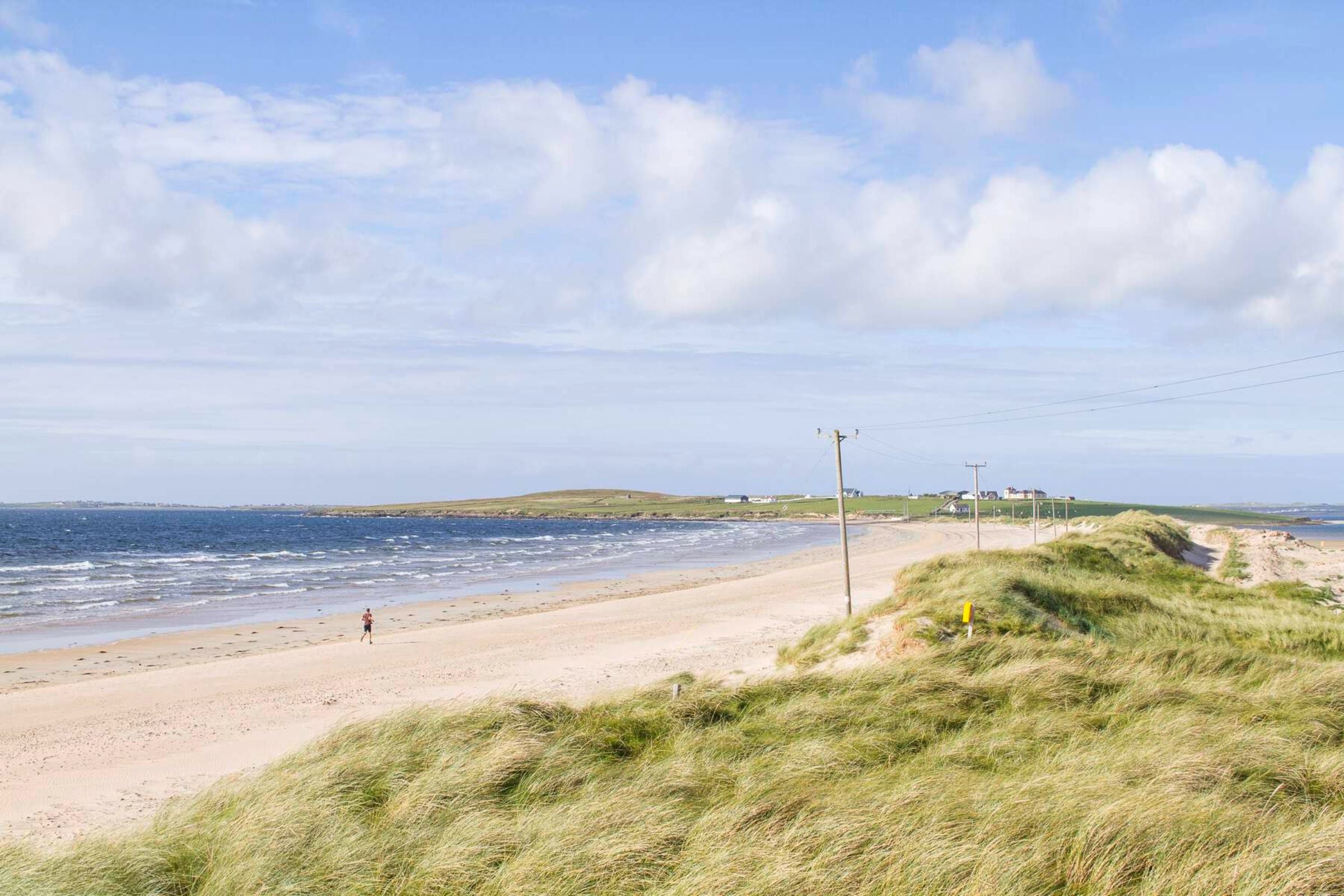 A sandy beach with grassy dunes and bright blue water lapping the shores.