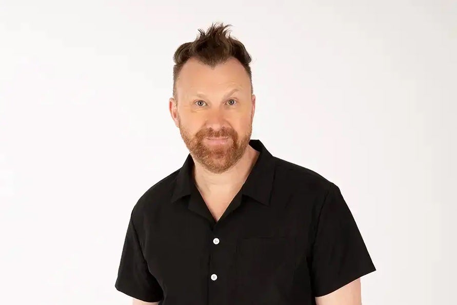 Smiling man in dark shirt against white background.