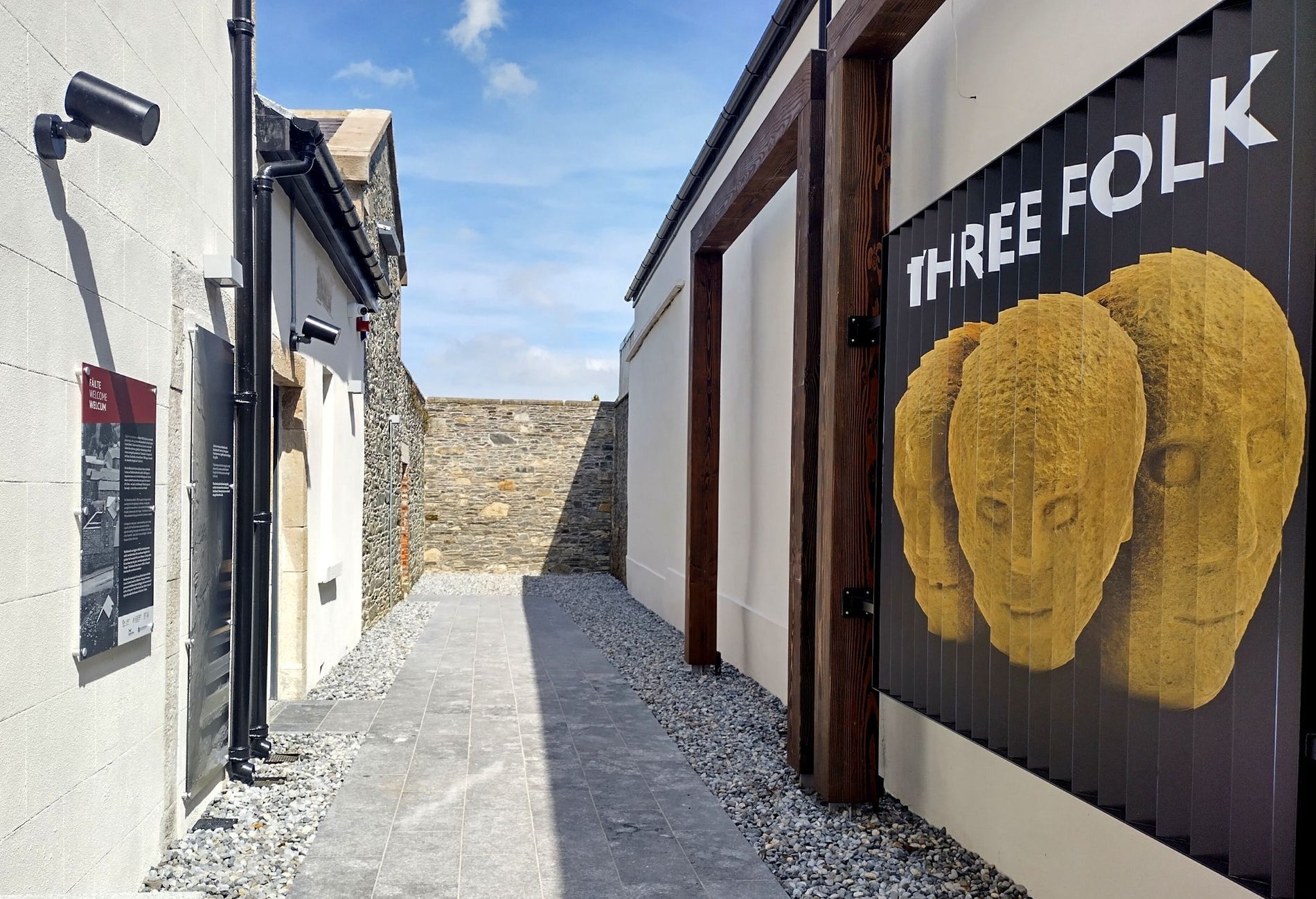An alleyway with an entrance to a visitor centre with a large wall mural of three stone heads