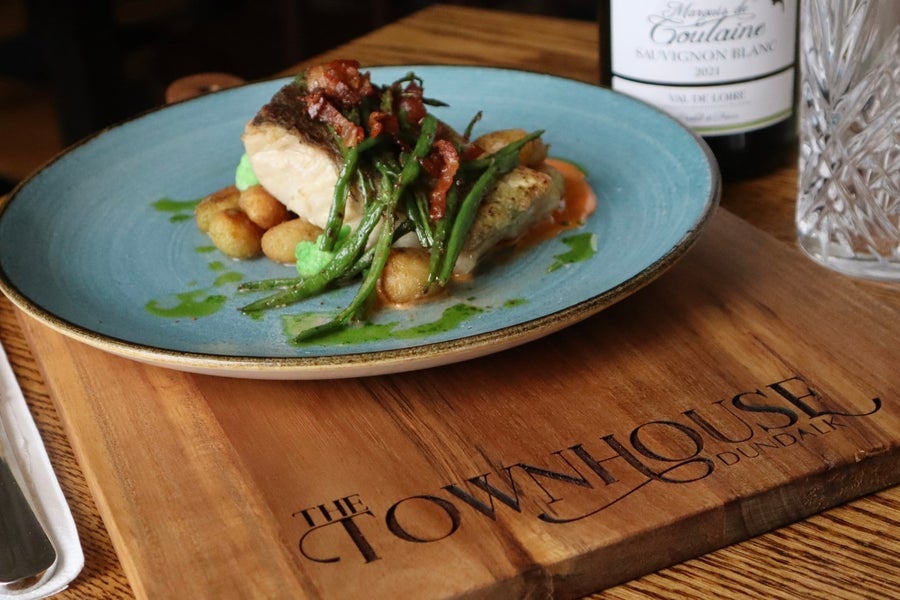 A chicken dish on a plate resting on a wooden slab with a restaurant name on it