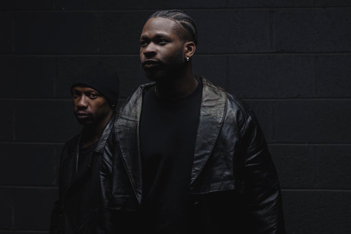 Very darkly lit photo of 2 men in dark clothing so barely visible.