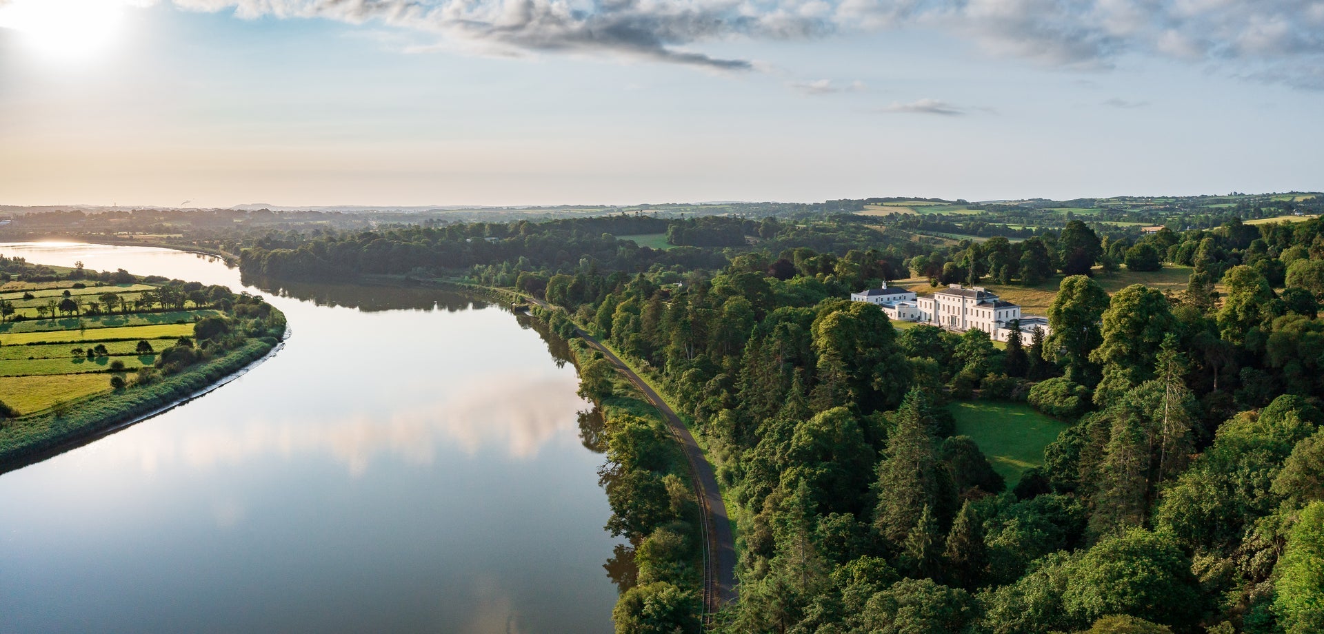 Aerial view of large estate house surrounded by trees and a lake in front