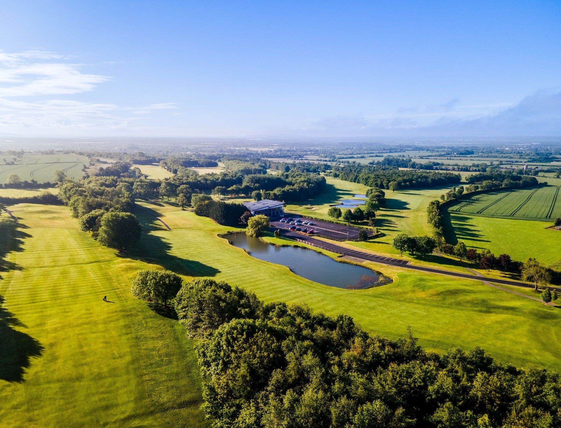An aerial view of a golf course and lake hazard on a sunny day