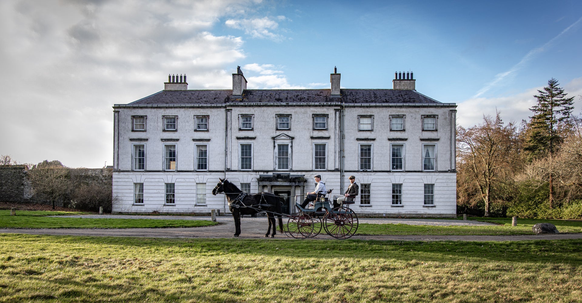The exterior of a large country house with a horse and carriage outside the entrance