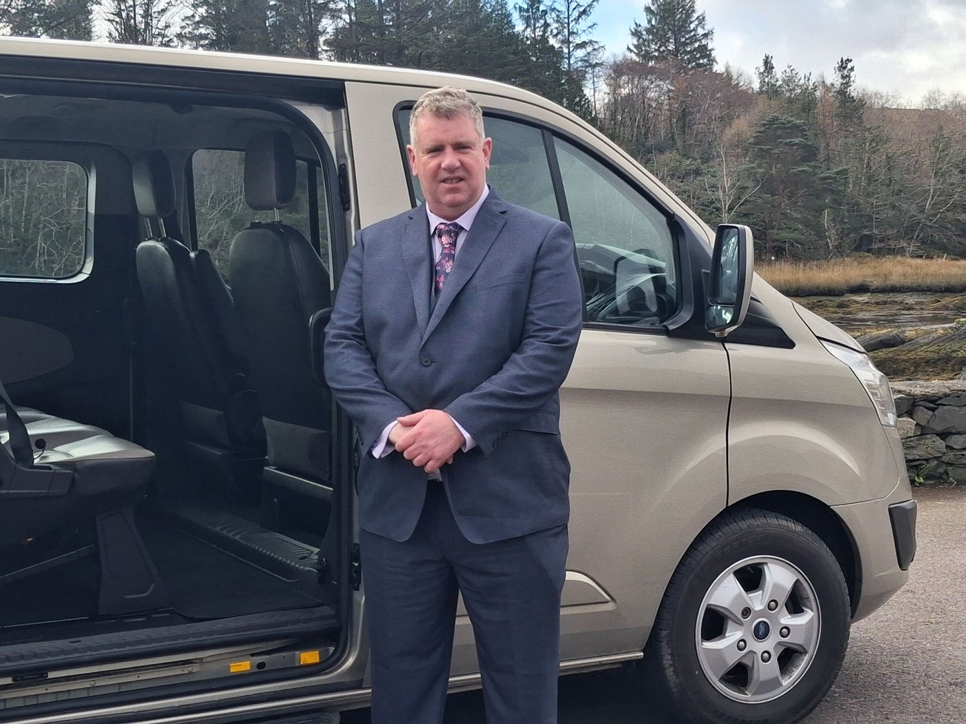 A chauffeur in a suit posed at his mini van