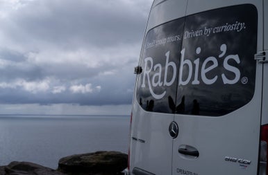 A small tour bus with a business logo parked beside the coast