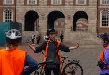 A lady standing in front of a bicycle wearing an orange high visibility vest and helmet