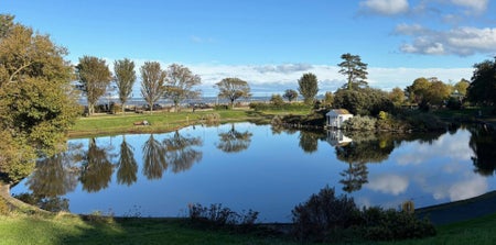 A clear lake surrounded by green trees reflects the blue sky above