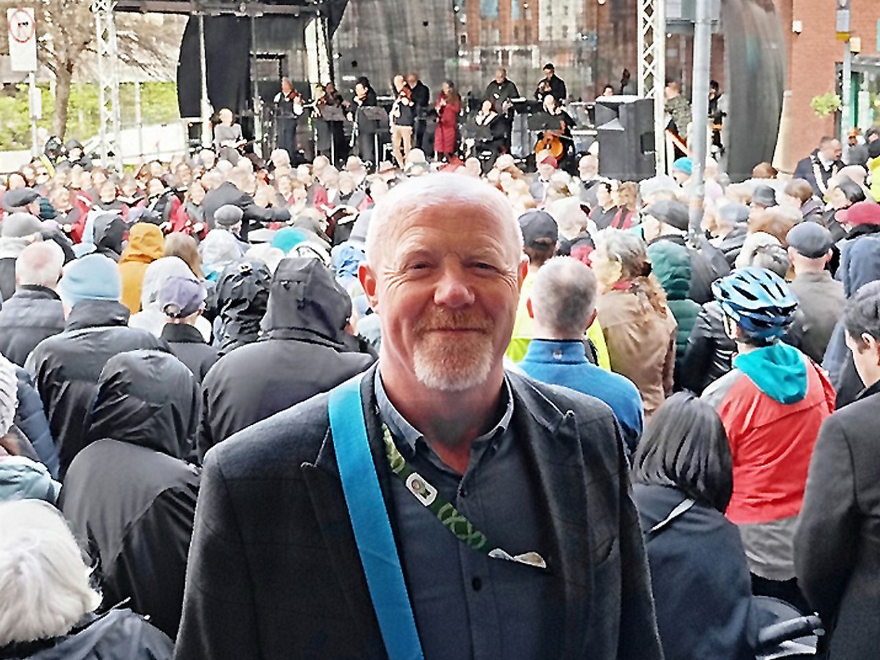 A person standing in front of a large outdoor crowd gathered at a stage with musicians performing