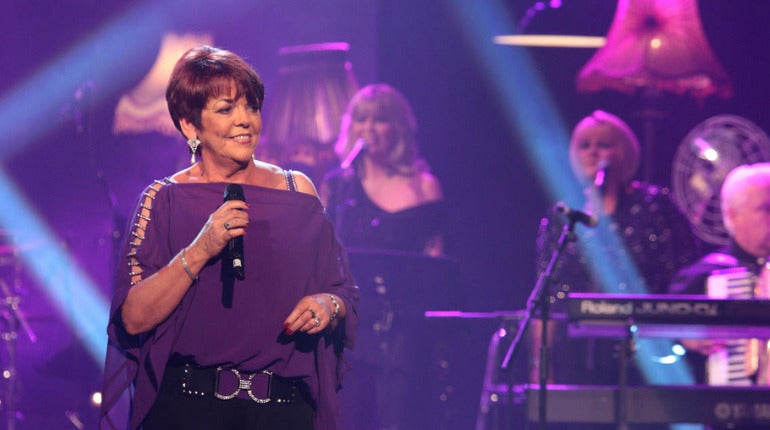 A smiling woman in purple dress holding a mic