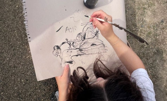 Looking down at young child holding a pen creating a black pen and ink picture.