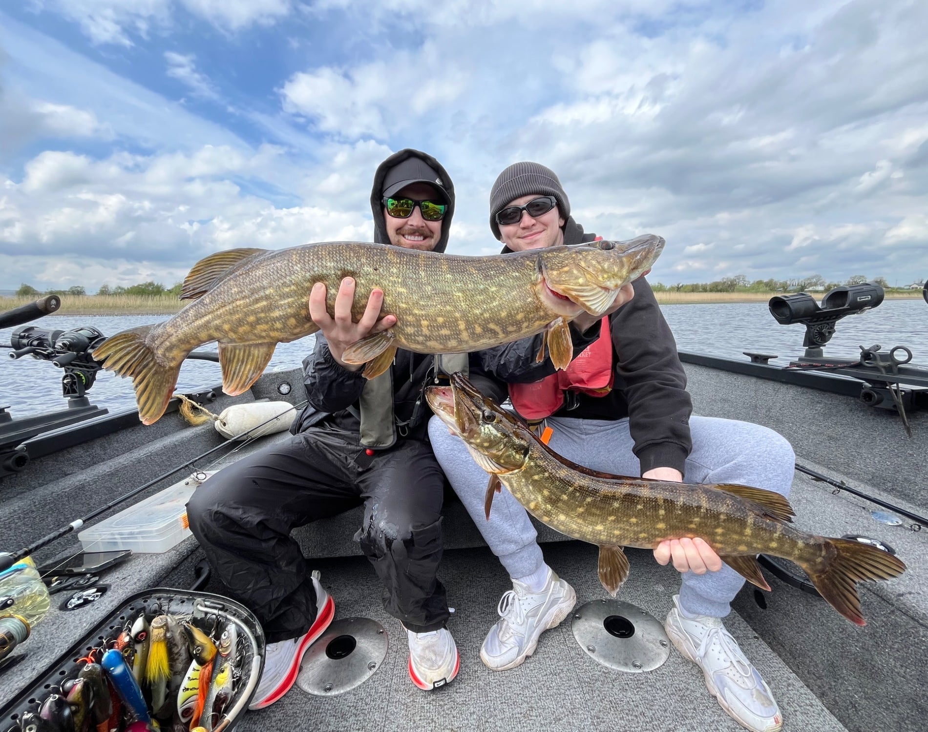 Two anglers holding large pike aboard a fishing boat on a lake