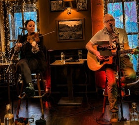 Live traditional Irish music performance featuring a fiddle player and guitarist in a cosy pub setting