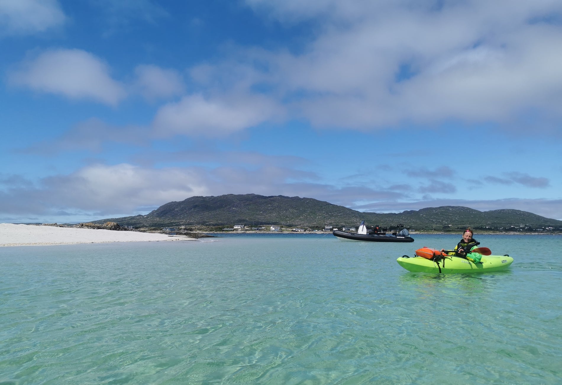 Person in a green kayak at sea near a sandy beach and green landscape