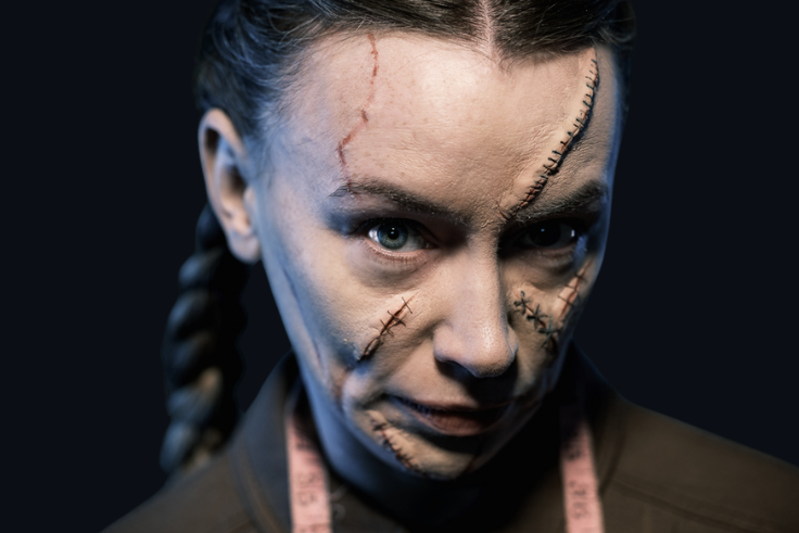 A woman with scarred SFX makeup looks sinisterly into the camera