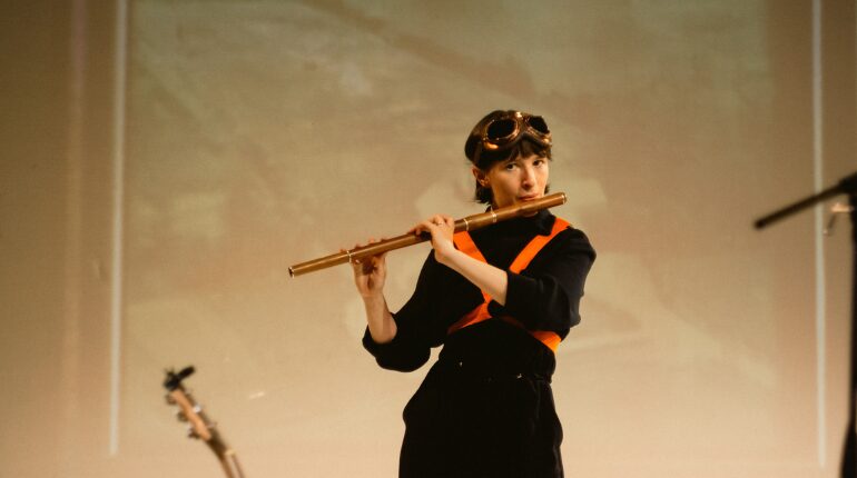 A woman dressed in black playing a wooden coloured flute