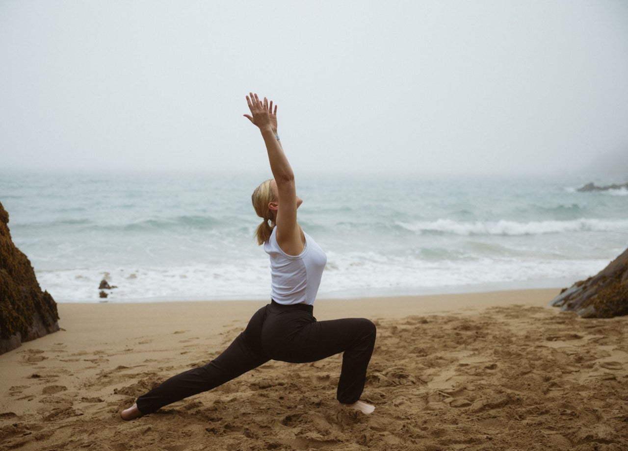 Lady doing a yoga stretch on the beach with the sea in the background