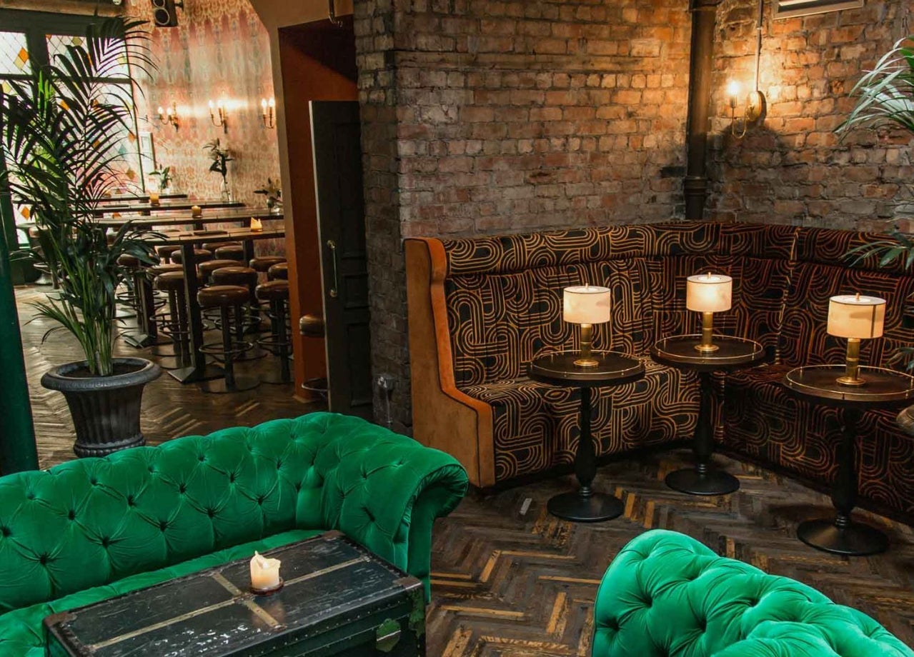 Green velvet seating area in an inviting lounge with candlelit tables and exposed brick walls