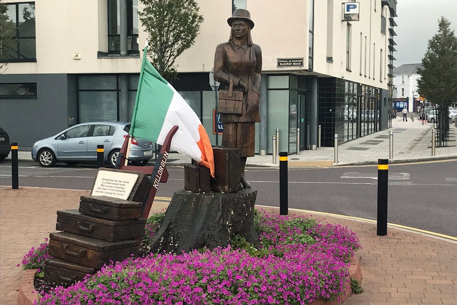 Sculpture in the form of a woman carved from an old oak tree with two suitcases alongside her