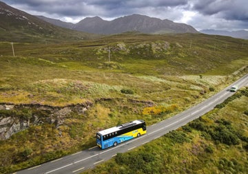 A blue and yellow coloured bus driving through Connemara countryside